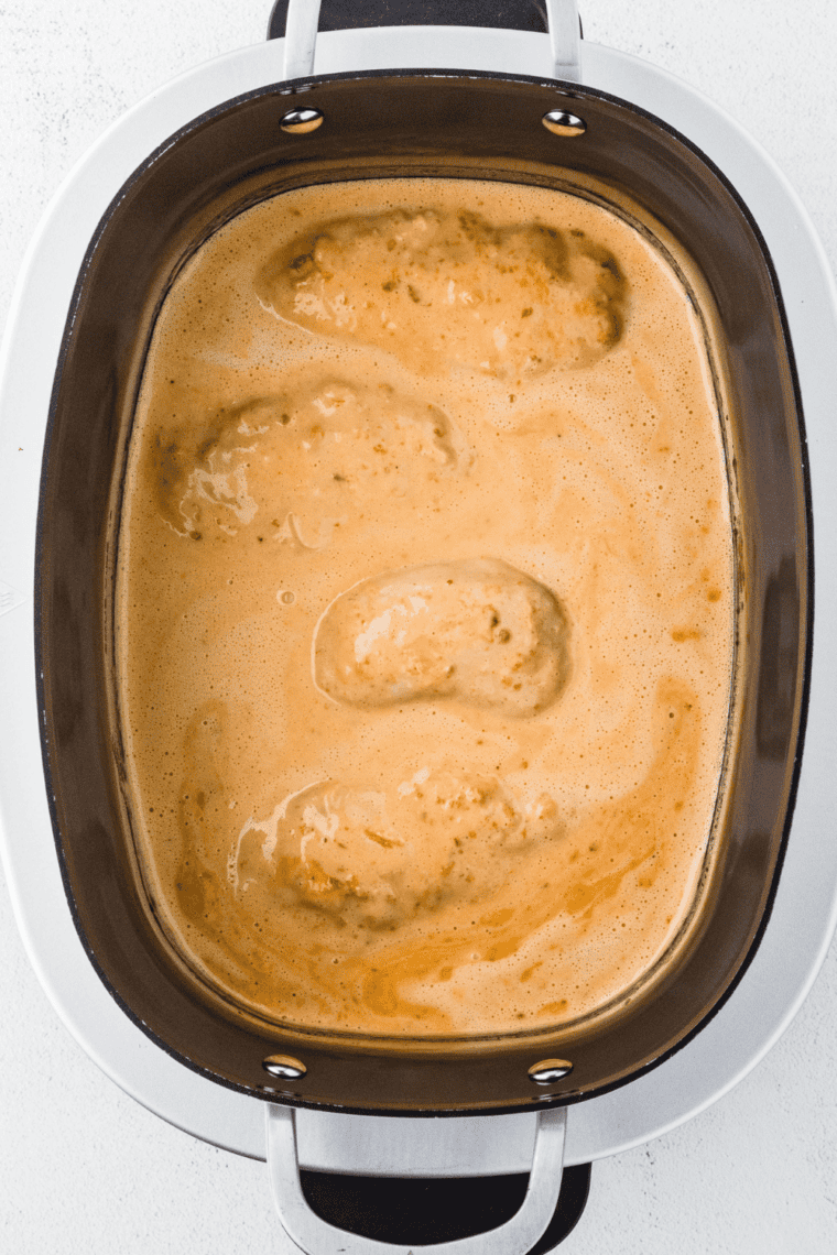 Slow cooker filled with chicken cooking in creamy bang bang sauce.