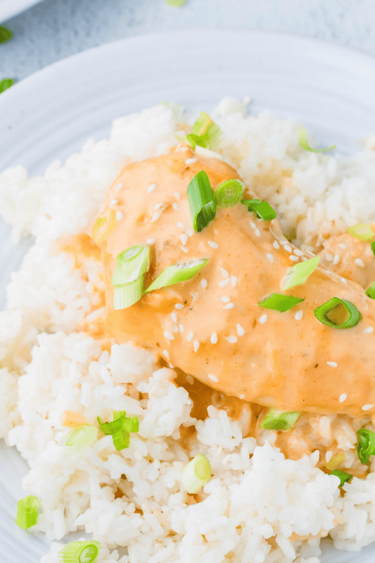 Shredded slow cooker bang bang chicken served over rice with creamy sauce and green onions.