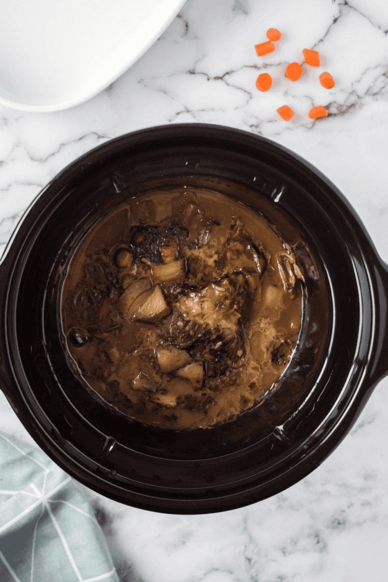 Beef roast cooking on top of vegetables in slow cooker until tender.