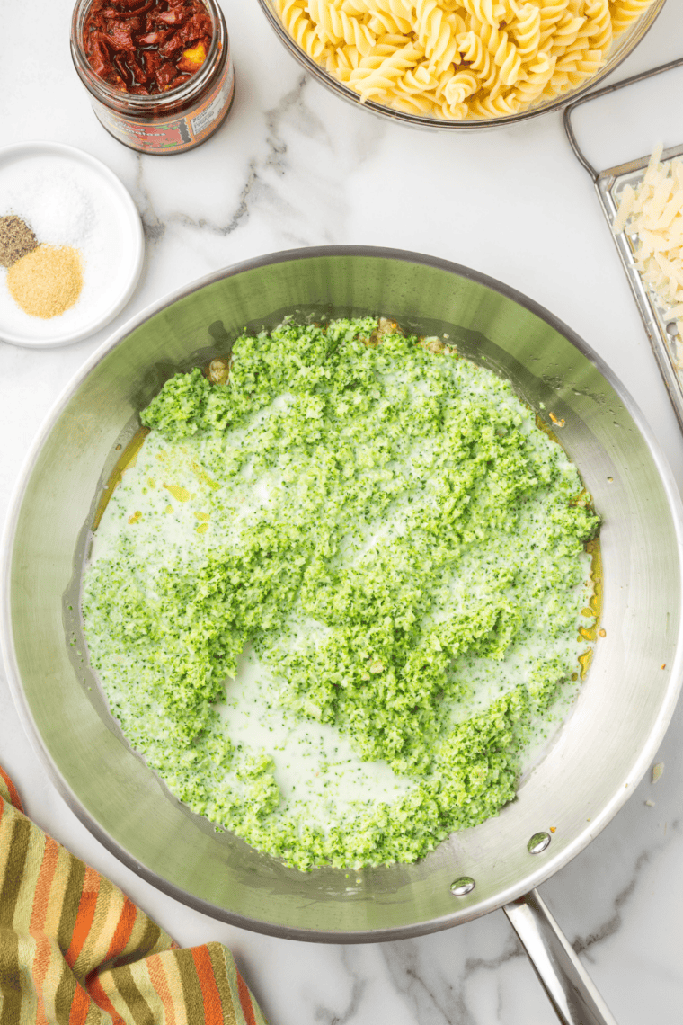 Stirring cooked pasta, sun-dried tomatoes, and parmesan into broccoli sauce, then folding in fresh basil.