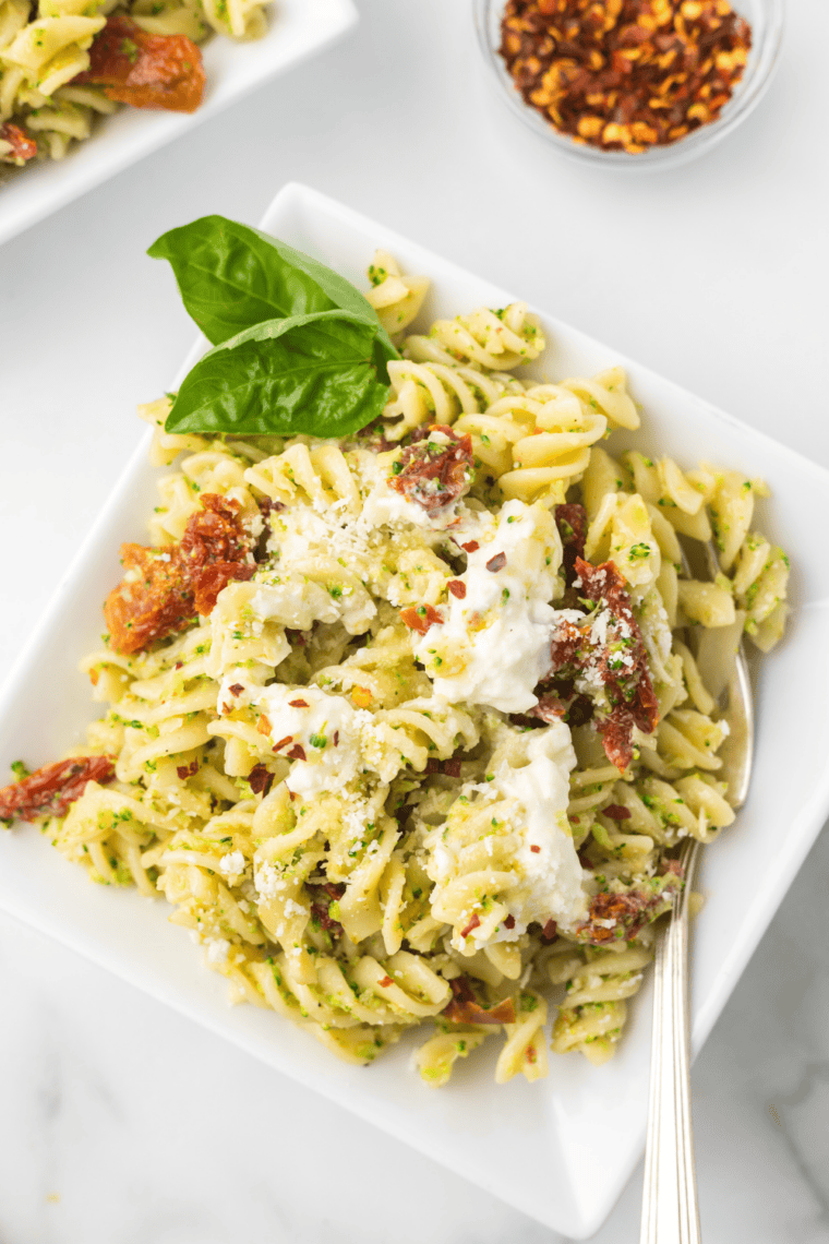 Cheesy broccoli fusilli pasta bake with sun-dried tomatoes and melted burrata in a casserole dish.