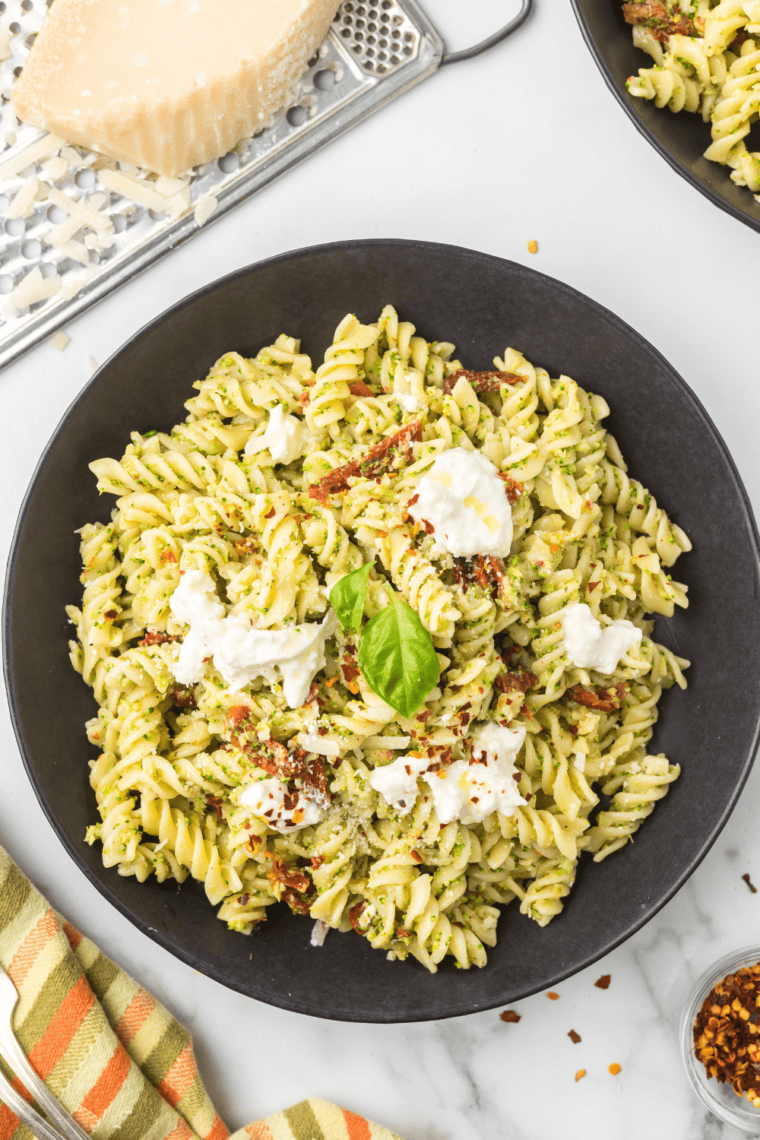 Cheesy broccoli fusilli pasta bake topped with melted burrata and sun-dried tomatoes in a casserole dish.