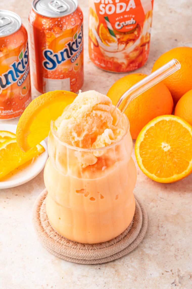 Tall glass of Ninja Slushi Frozen Dirty Orange Soda with straw, orange slice garnish, and icy texture