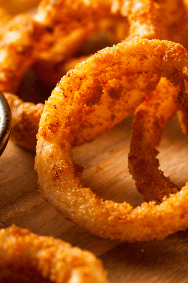 Golden crispy air fryer Long John Silver style onion rings served on a plate with dipping sauce.