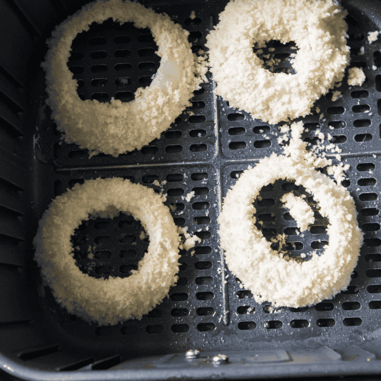 Battered onion rings in air fryer basket, golden brown and crispy, halfway through cooking.