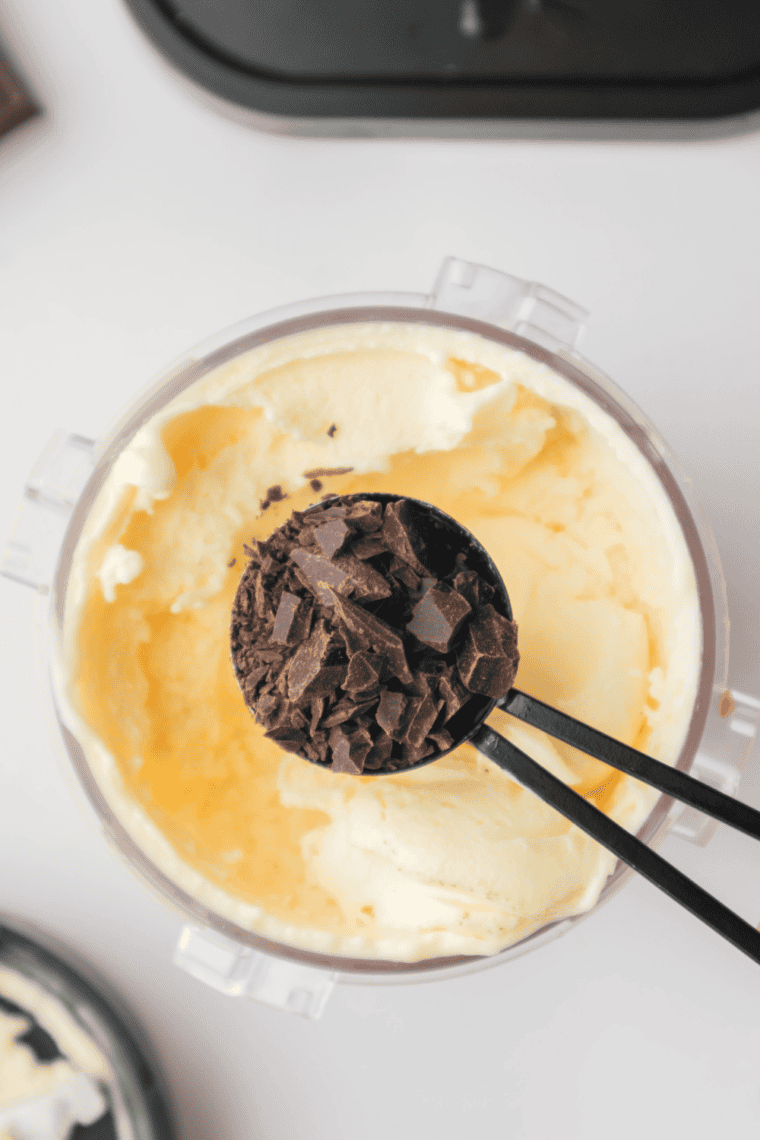 Folding chocolate chip cookie chunks into ice cream base for even distribution.
