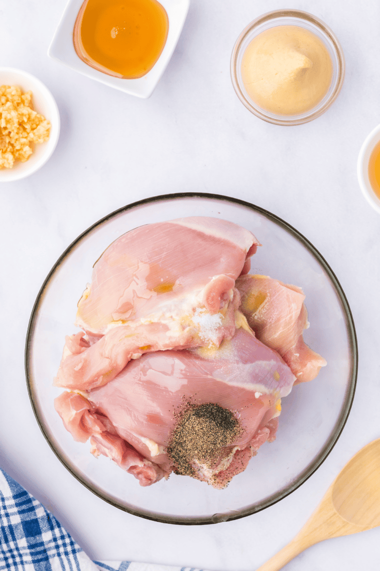 Boneless chicken thighs being coated with olive oil, salt, and pepper.
