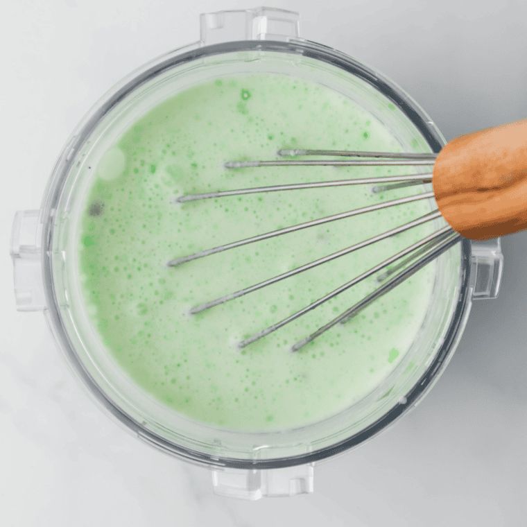 Whisking milk, cream, sugar, peppermint extract, and green food coloring in a bowl.