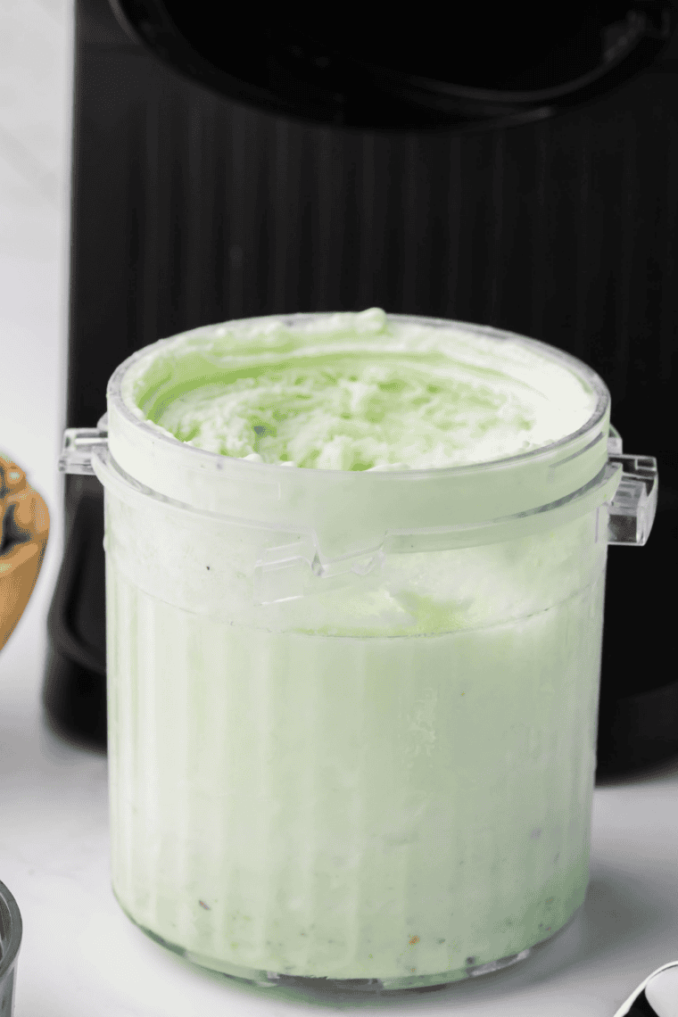 Scooping bright green mint ice cream into a bowl with festive toppings.