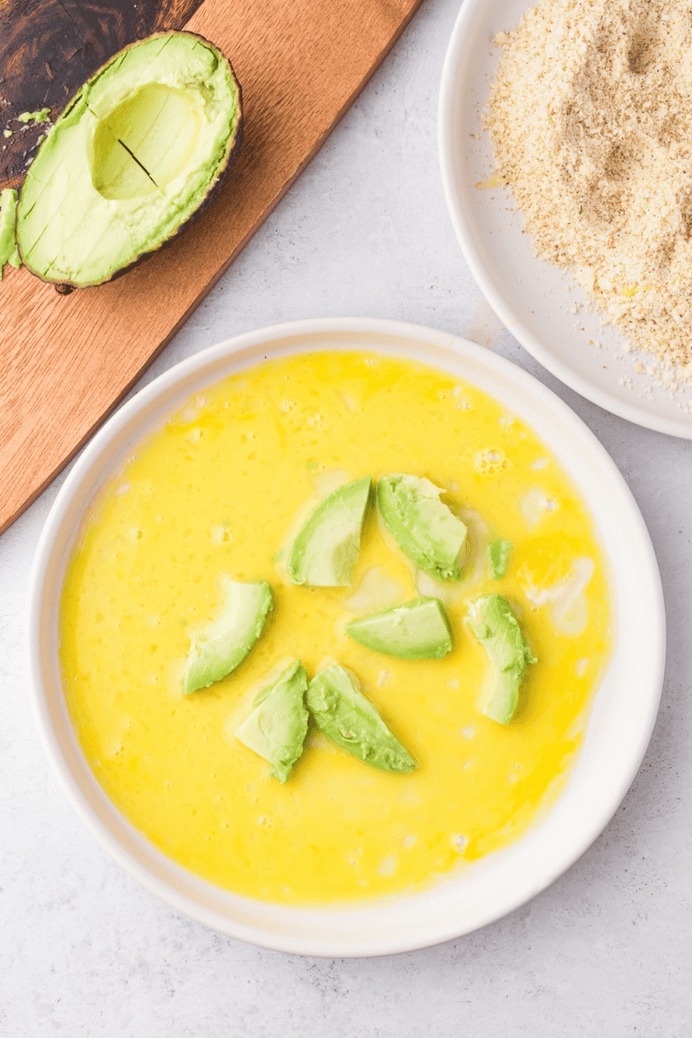 avocado cubes being dipped in beaten egg and rolled in seasoned breadcrumbs