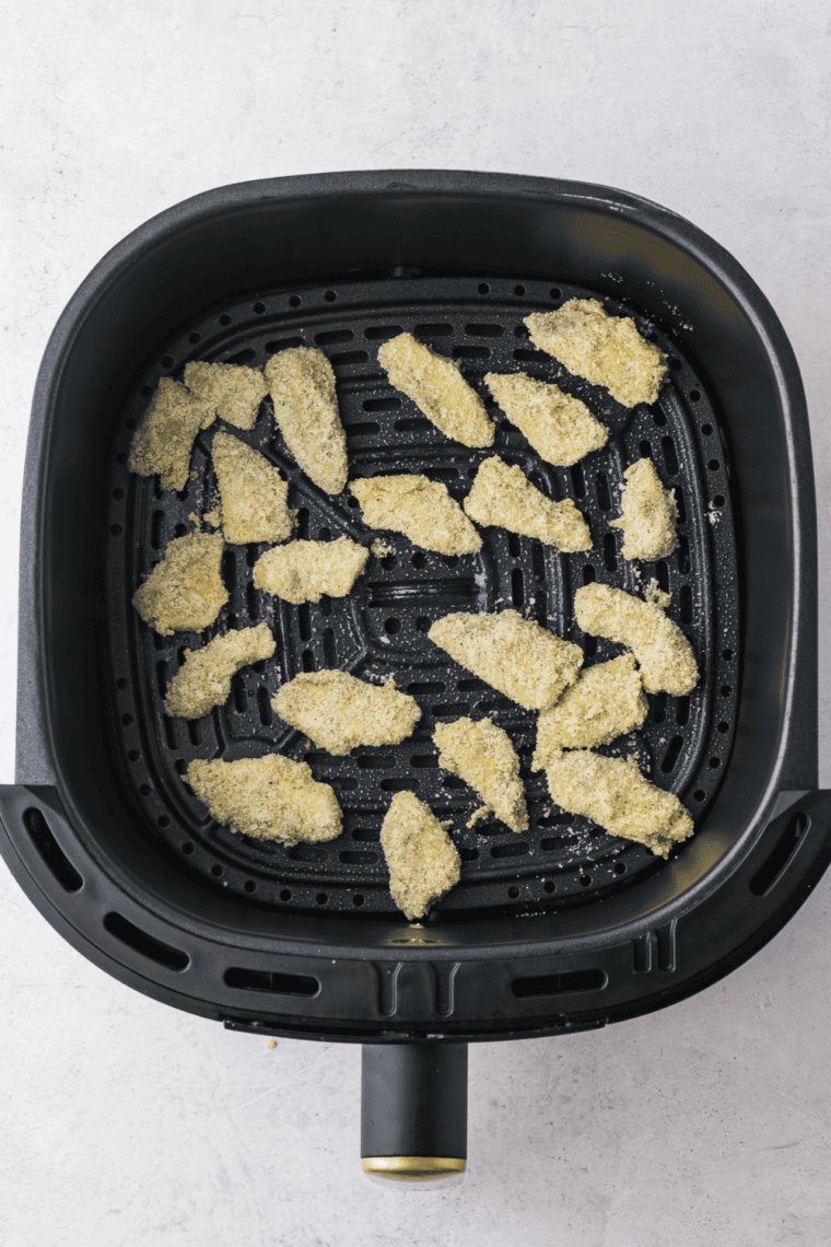 avocado cubes arranged in air fryer basket cooking until golden and crispy