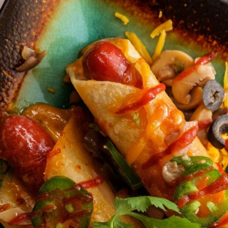 Hot dog taquitos resting after air frying with melted cheese inside.