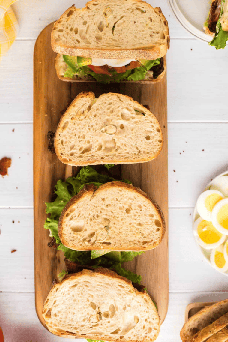 Close-up of a BLTE sandwich with crispy bacon, lettuce, tomato, and a fried egg stacked on toasted bread served on a plate.