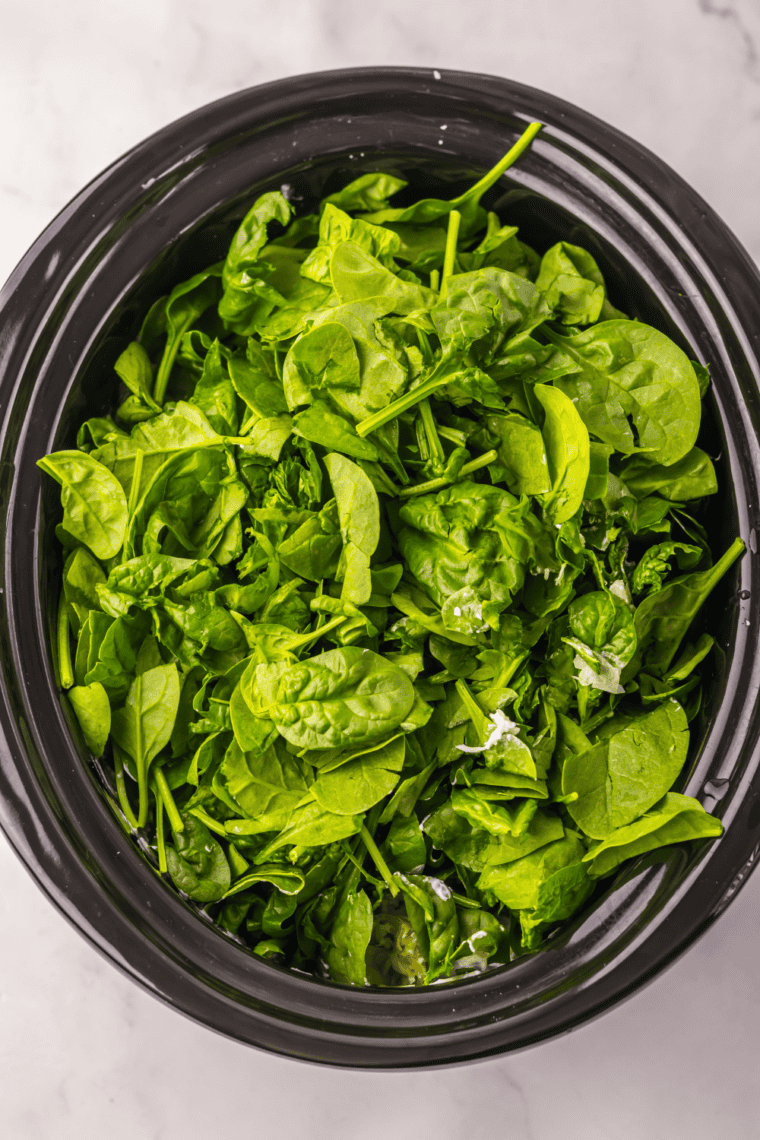 Ingredients added to crockpot including spinach cheeses and seasonings for dip