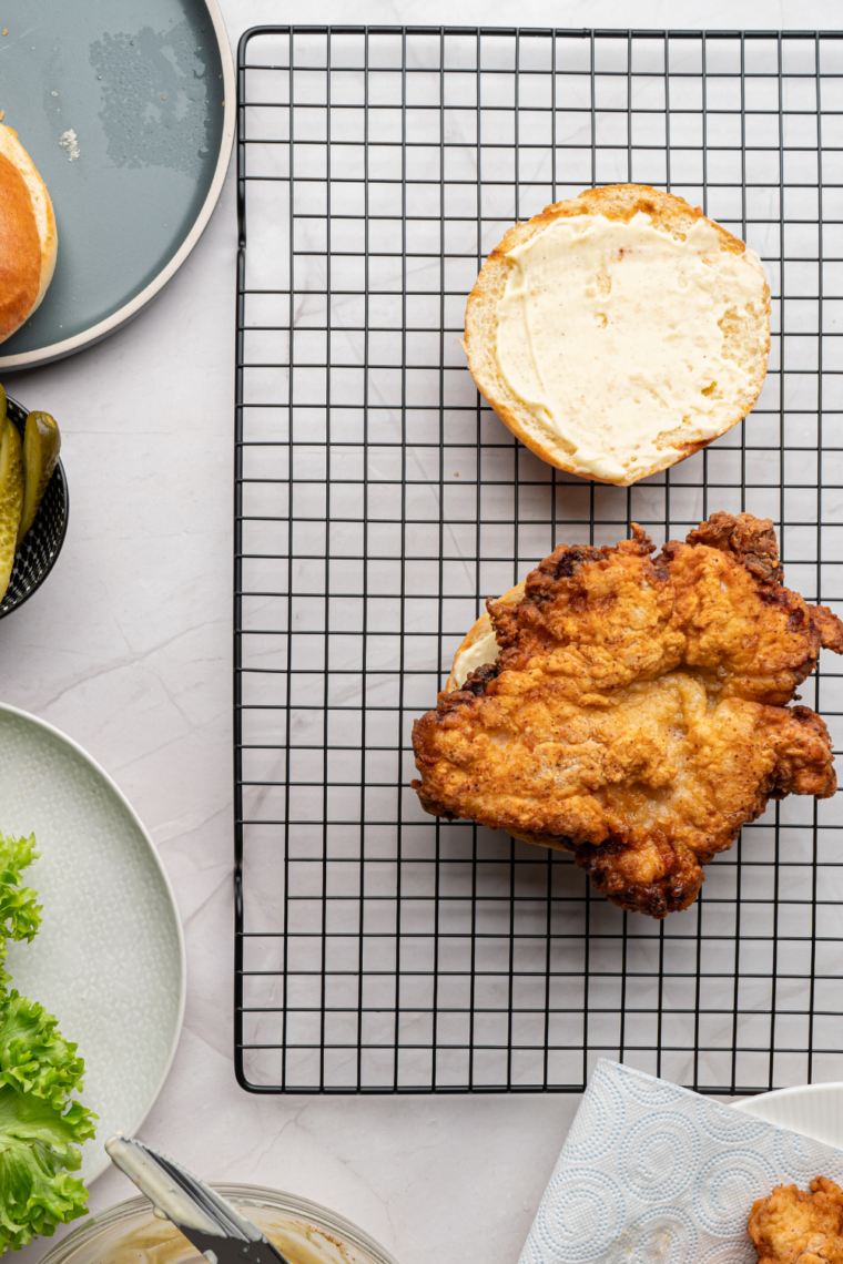 Close-up of crispy fried chicken sandwich with craggy coating, pickles, and mayo on a brioche bun.