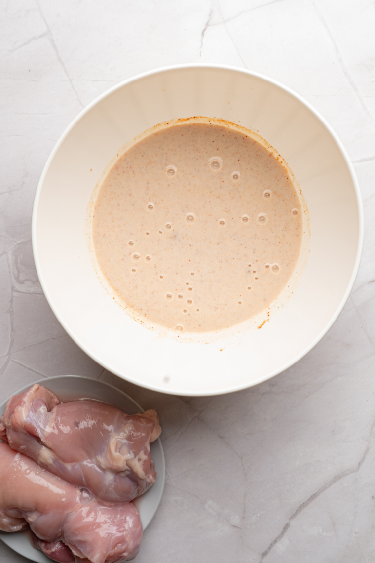 Chicken fillets soaking in buttermilk marinade with hot sauce, egg, and spices in a mixing bowl, covered and chilled for tender juicy fried chicken preparation.
