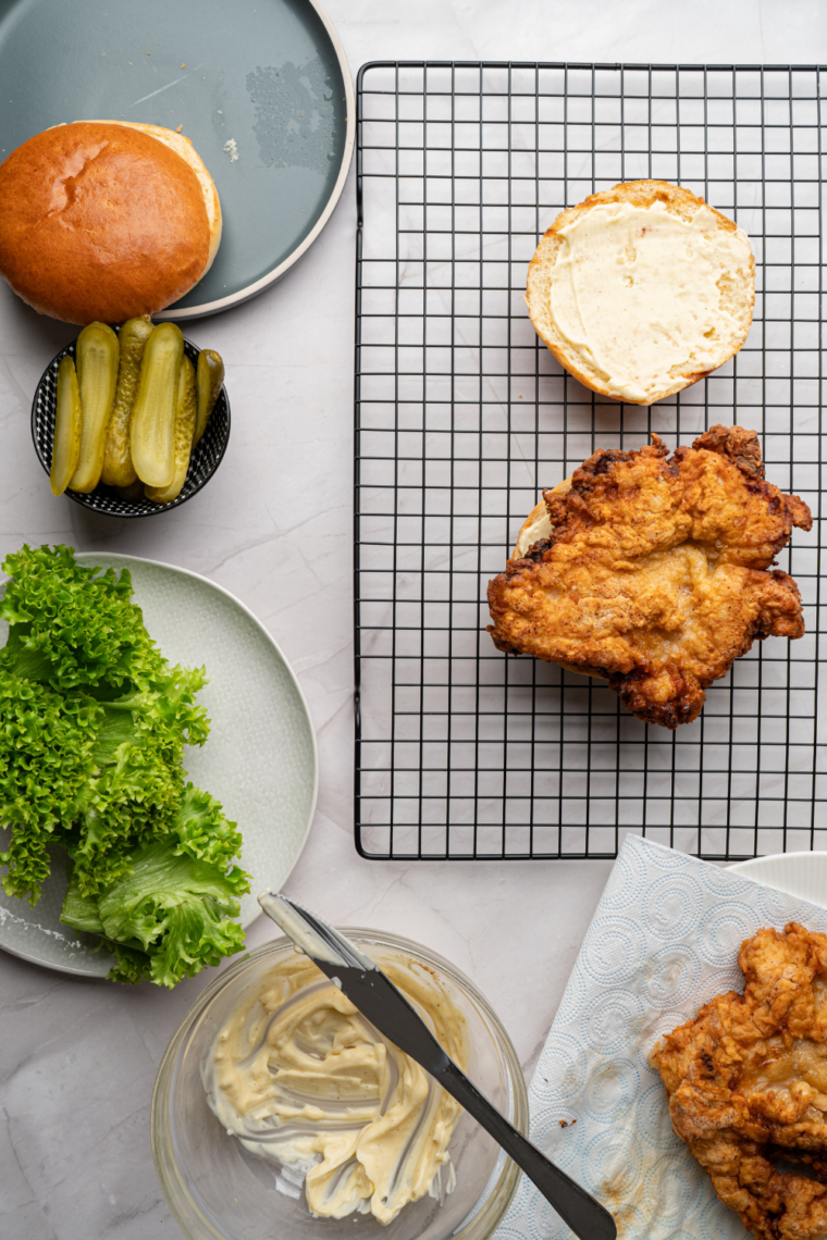 Chicken fillet being pressed into seasoned breading mixture, coated thoroughly with craggy crumbs, then rested on a rack before frying for extra crispy texture.