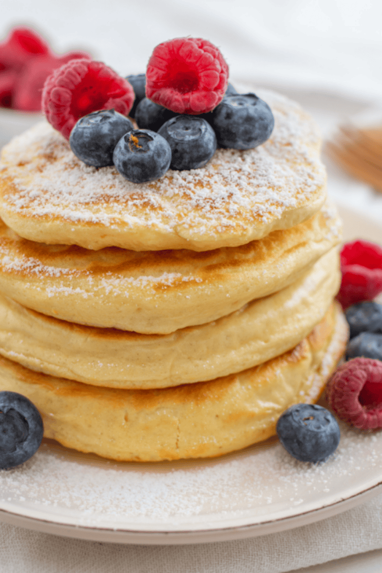 Stack of fluffy golden Perkins-style pancakes topped with butter and maple syrup served on a white plate in classic diner breakfast presentation.