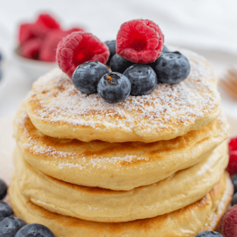 Stack of fluffy golden Perkins-style pancakes topped with butter and maple syrup served on a white plate in classic diner breakfast style presentation.