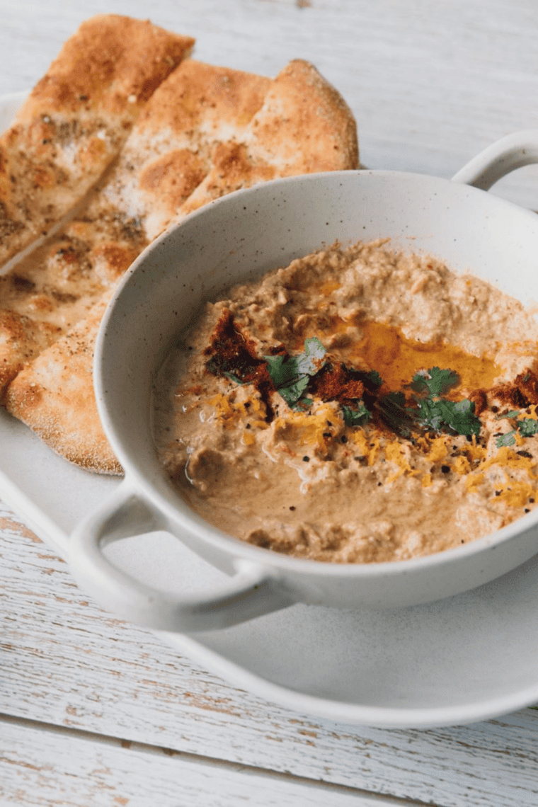 Creamy roasted eggplant dip in bowl with olive oil and herbs served as Mediterranean appetizer with pita bread and vegetables