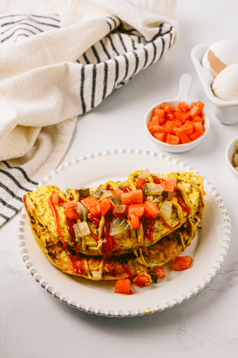 Loaded First Watch The Works Omelet with eggs, bacon, ham, sausage, peppers, onions, mushrooms, and melted cheese on a plate