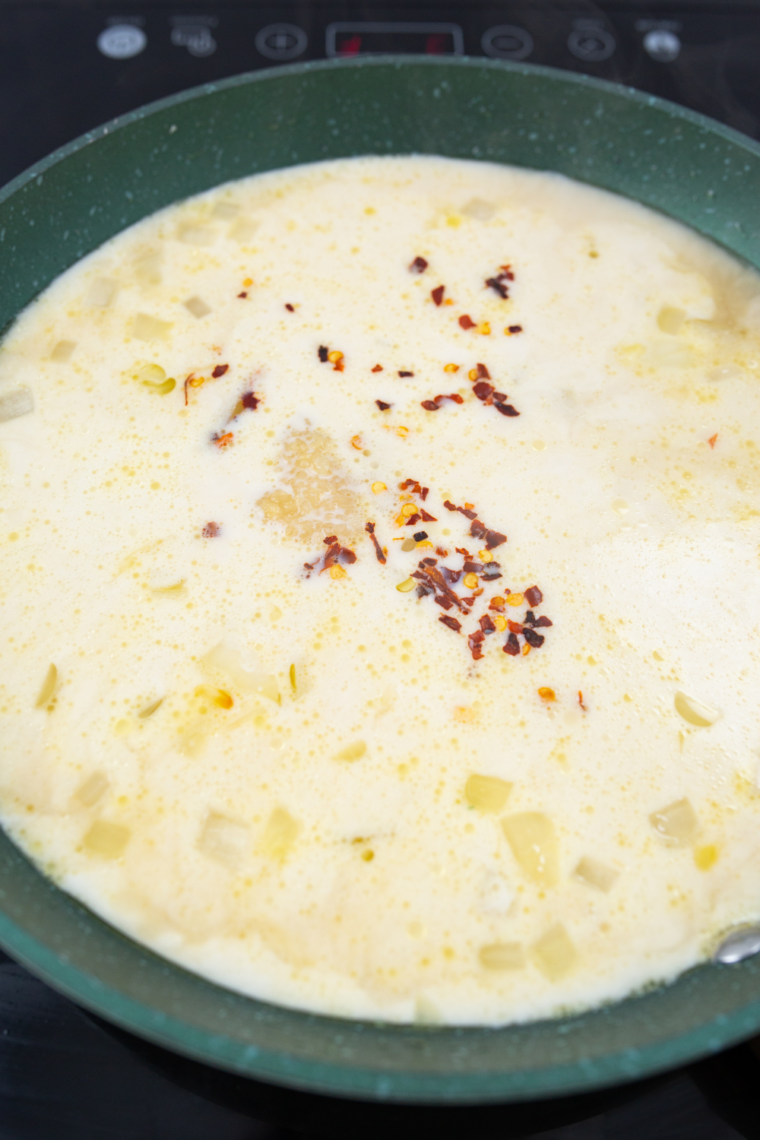 Assembling baked pasta with chicken, broccoli, tomatoes, and Alfredo sauce topped with cheese