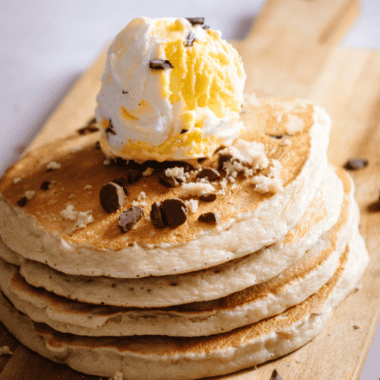 Stack of fluffy chocolate chip pancakes topped with melting chocolate chips and syrup on a white plate styled like First Watch breakfast presentation.