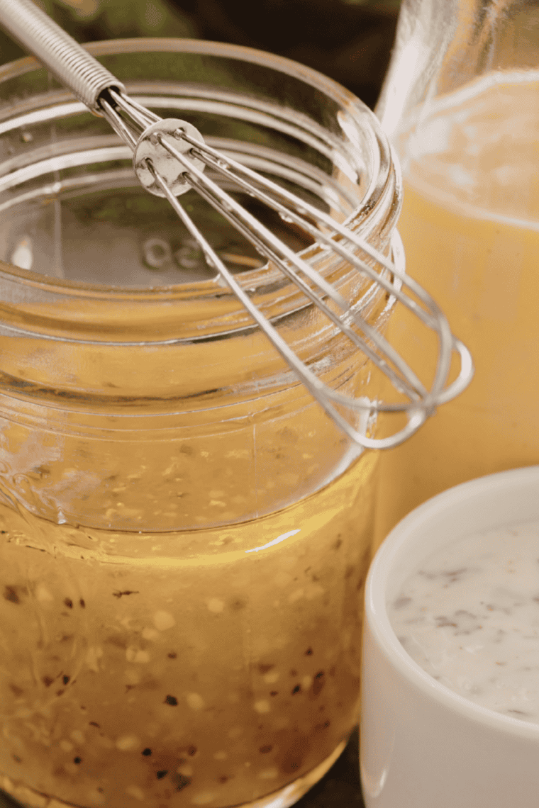 Glass jar of homemade lemon dressing made with fresh lemon juice, olive oil, and honey served with a fresh green salad and lemon slices on the side.