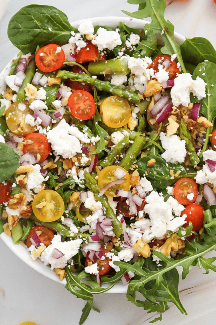 Glass jar of homemade lemon dressing made with fresh lemon juice, olive oil, Dijon mustard, and herbs served beside a fresh green salad with lemon slices.