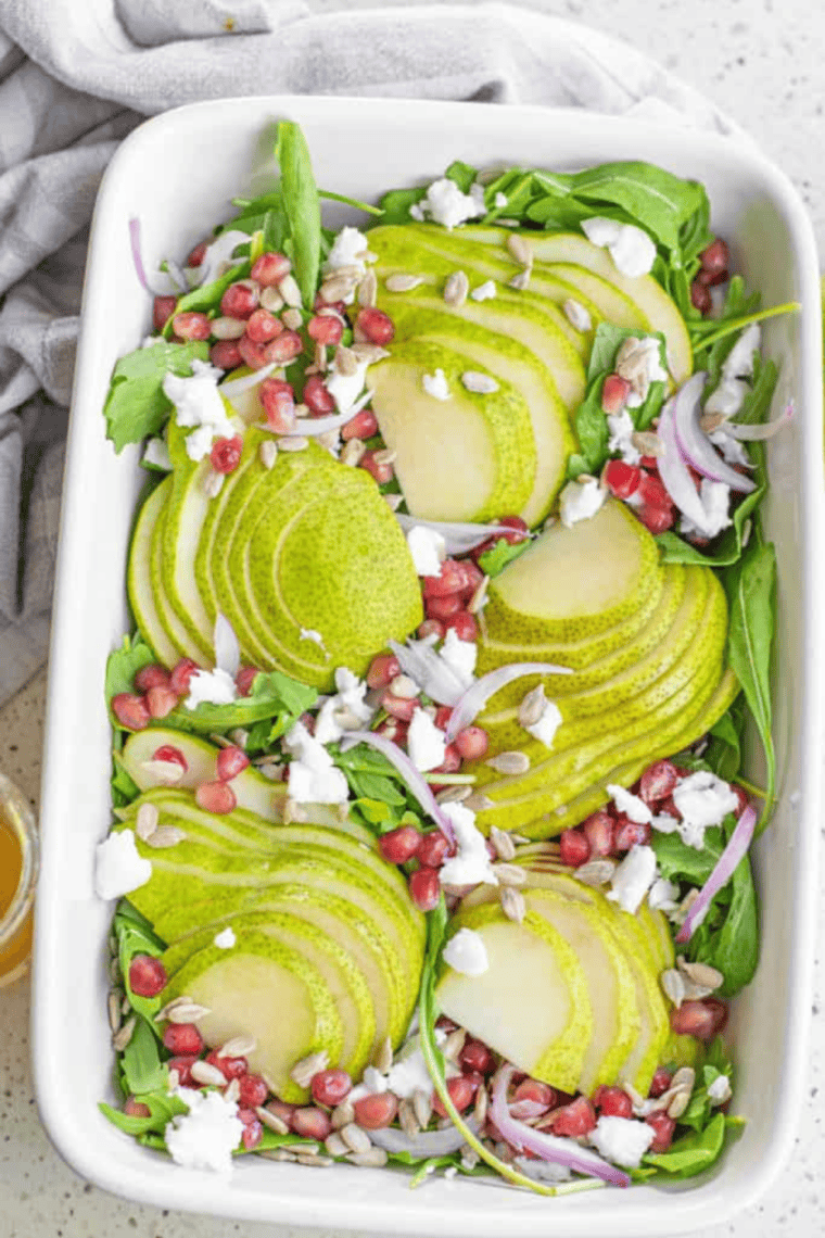Glass jar of homemade lemon dressing made with fresh lemon juice, olive oil, Dijon mustard, garlic, and herbs served with a fresh green salad and lemon slices on a white plate.