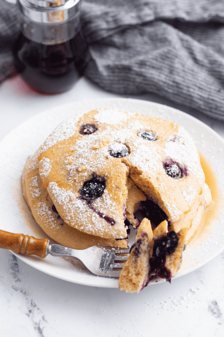 Stack of fluffy lemon ricotta pancakes topped with powdered sugar, fresh berries, and syrup on a white plate for a brunch-style breakfast.