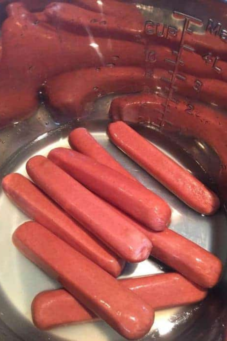 Instant Pot filled with 1 cup water and steamer basket holding hot dogs standing upright for even steaming and maximum capacity.