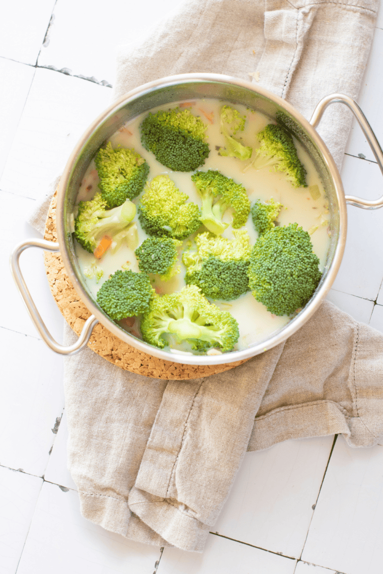Broccoli florets and sliced carrots simmering in creamy soup until tender