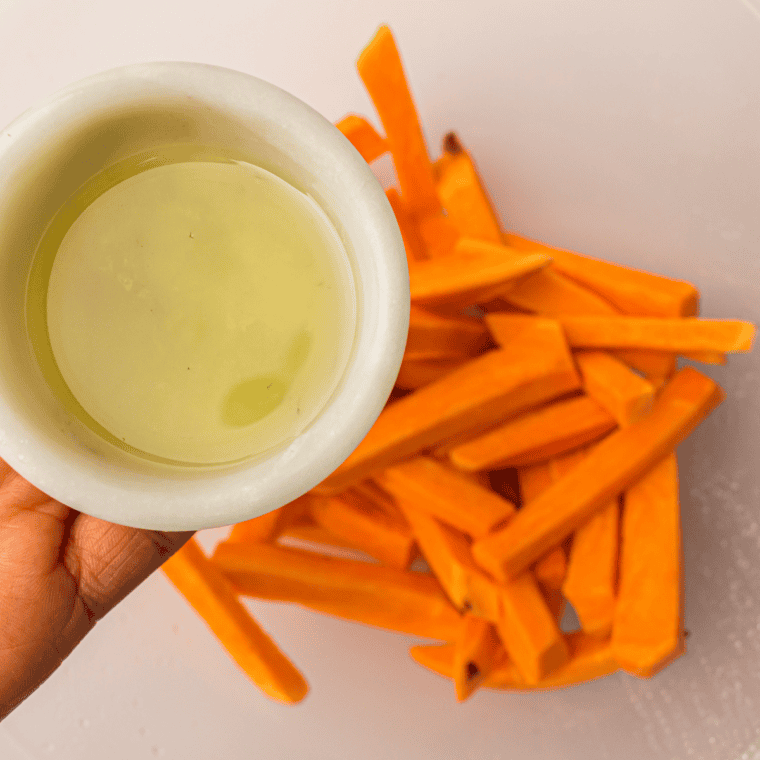 Sweet potato fries tossed in olive oil, salt, pepper, and paprika in a bowl.