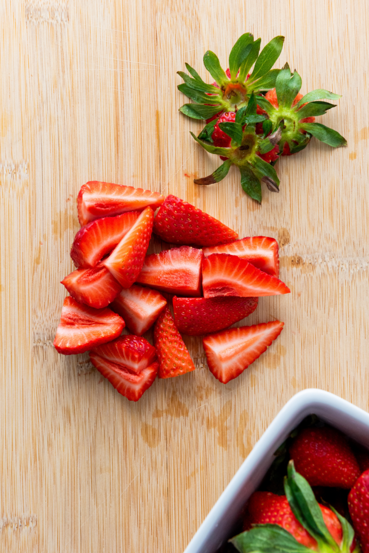 Fresh strawberries being rinsed hulled and cut into quarters in a bowl