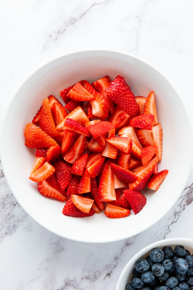Blueberries added to strawberries in a mixing bowl and gently tossed