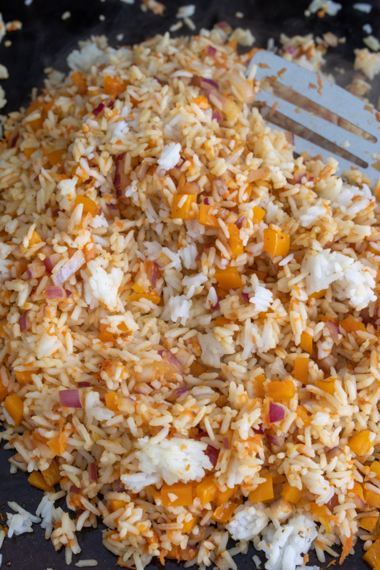 Cold rice spread flat on hot griddle developing crispy golden fried rice texture