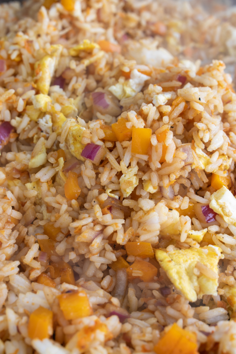 Blackstone fried rice cooking on flat top griddle with rice, eggs, peas, carrots, and soy sauce being tossed together.
