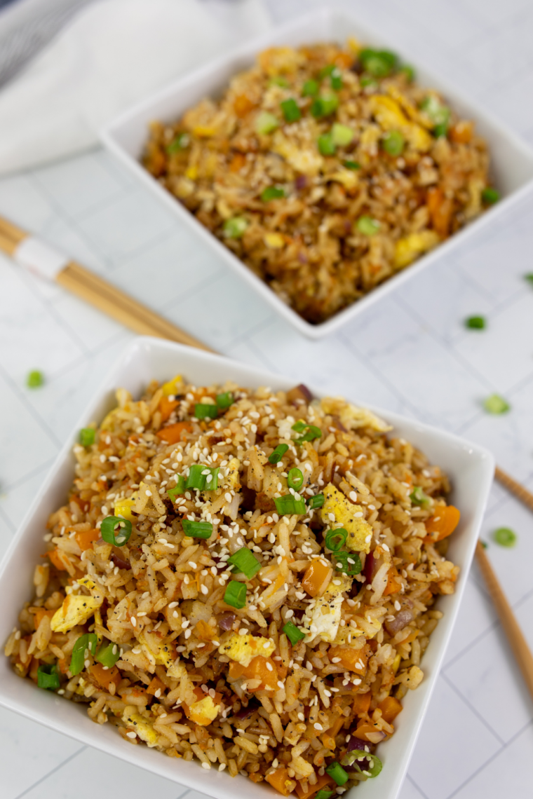 Close-up of fried rice on a Blackstone griddle with scrambled eggs, vegetables, and rice being mixed with spatulas.
