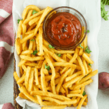 Bowl of homemade Zaxby&rsquo;s fry seasoning spice mix sprinkled over crispy golden fries on a rustic table.