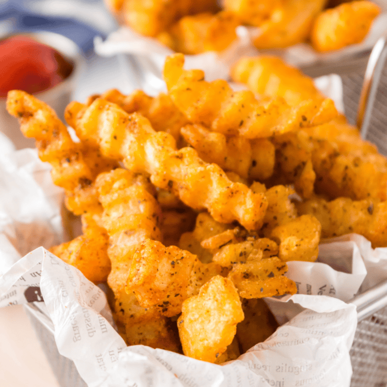 Crispy hot fries being sprinkled with seasoning straight from fryer, with spice mix stored in an airtight jar nearby.