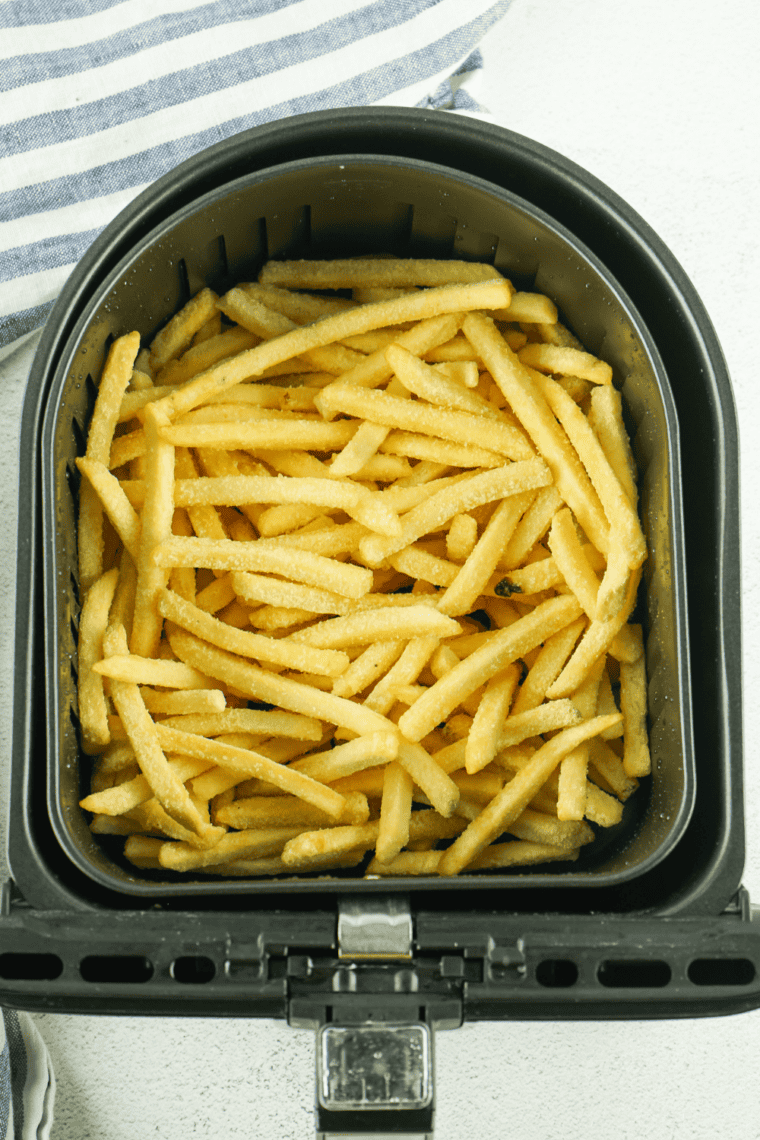 Small bowl of Zaxby&rsquo;s fry seasoning spice blend next to crispy golden fries being seasoned for extra flavor.