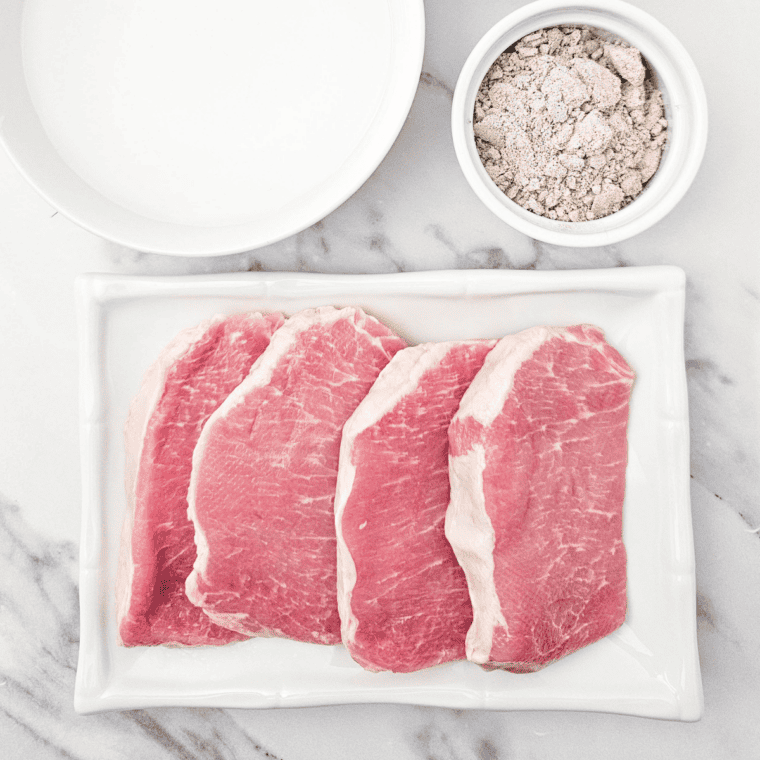 Pork chops, French onion soup mix packet, and a can of cream of mushroom soup on kitchen table.
