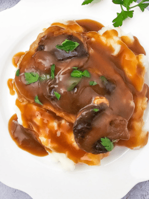 Slow cooker pork chops smothered in creamy mushroom and French onion sauce on a serving plate.