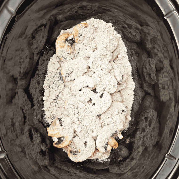 French onion soup mix packet being sprinkled evenly over raw pork chops in a crock pot.