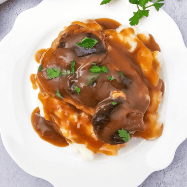 Slow cooker pork chops smothered in creamy mushroom and French onion sauce on a serving plate.