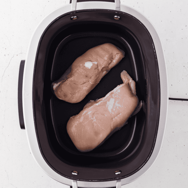 Raw boneless skinless chicken breasts arranged in a single layer in a 6-quart slow cooker for 4 ingredient chicken and stuffing