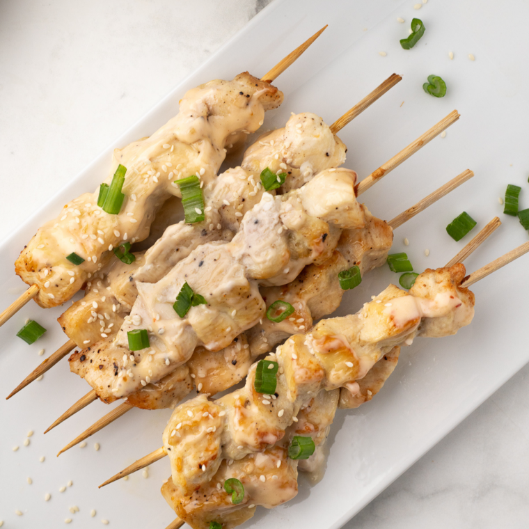 Golden chicken skewers brushed with bang bang sauce in air fryer basket