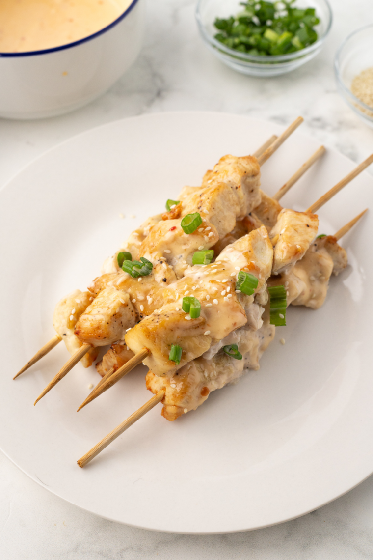 Close up of glazed chicken skewers topped with sesame seeds and green onions