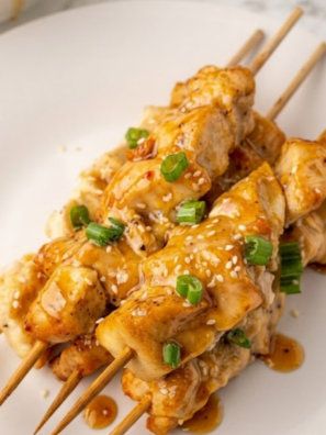 Golden air fryer bang bang chicken skewers coated in creamy spicy sauce served on a plate.